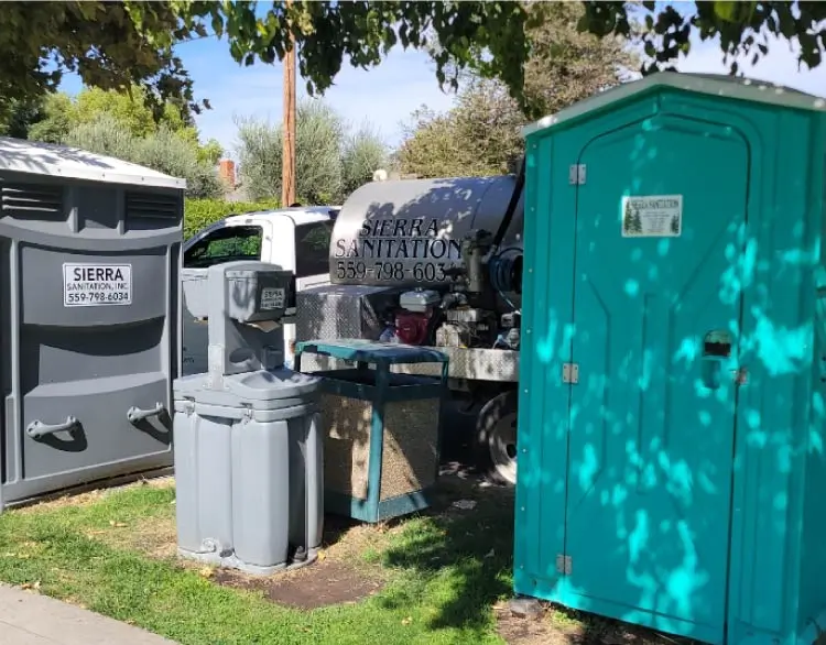 Sierra Sanitation septic pumping truck parked next to a green portable toilet and a handwashing station on a grassy area