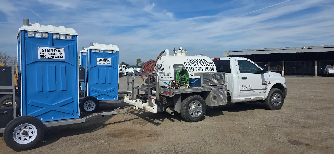 Sierra Sanitation white service truck with a septic pump tank towing a trailer with two blue portable toilets at the Visalia headquarters.