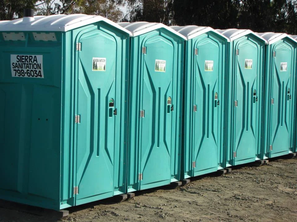 a row of teal standard porta potties